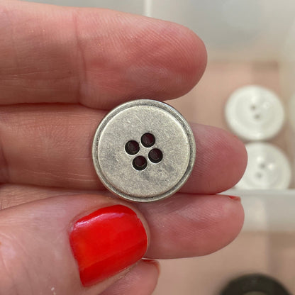 Hand holding a silver button with a clear container of buttons in the background