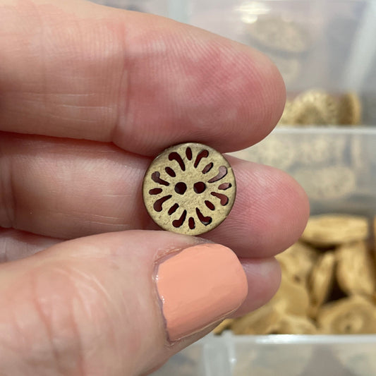 Gold button held between fingers with a container of buttons in the background