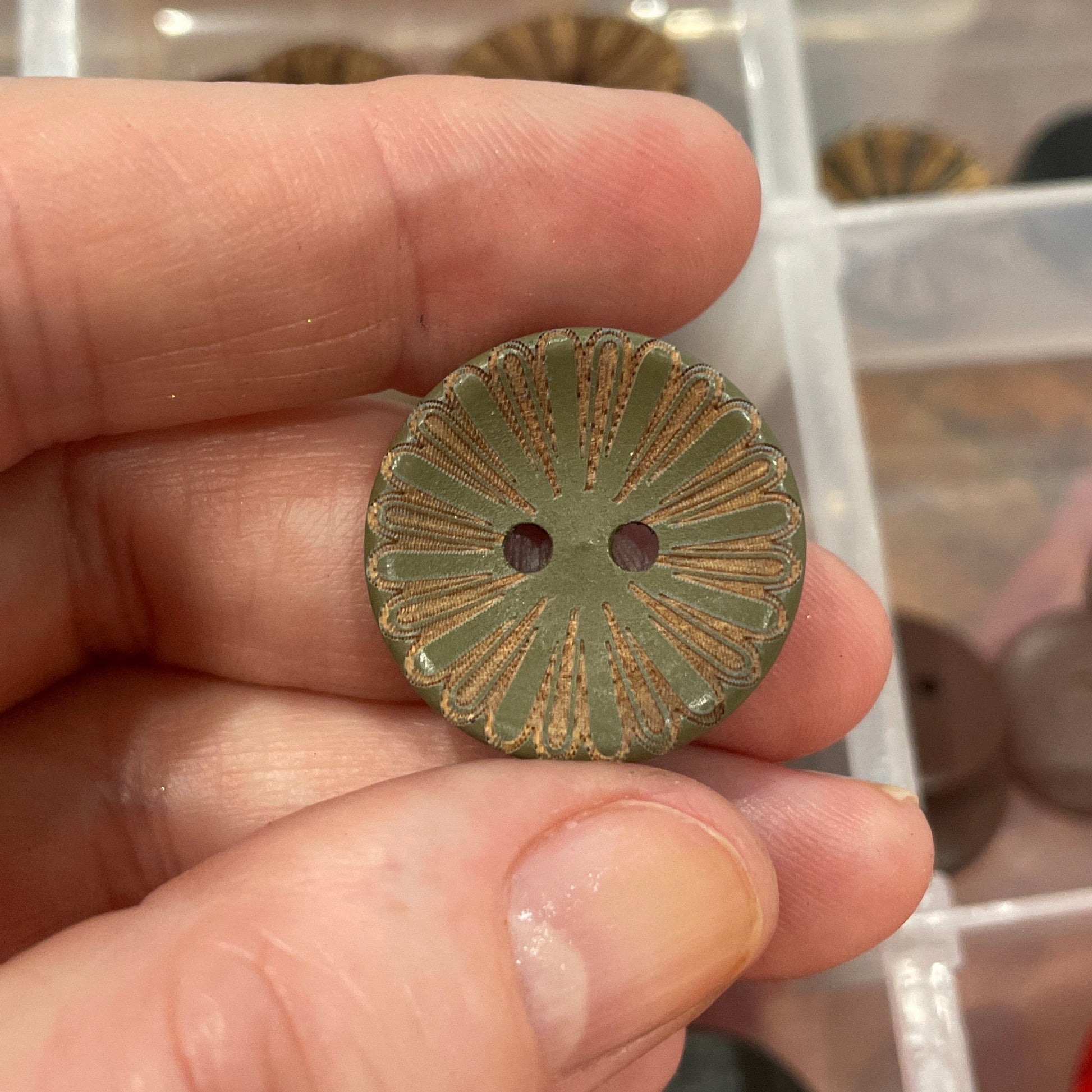 Hand holding a decorative button with a clear container of buttons in the background