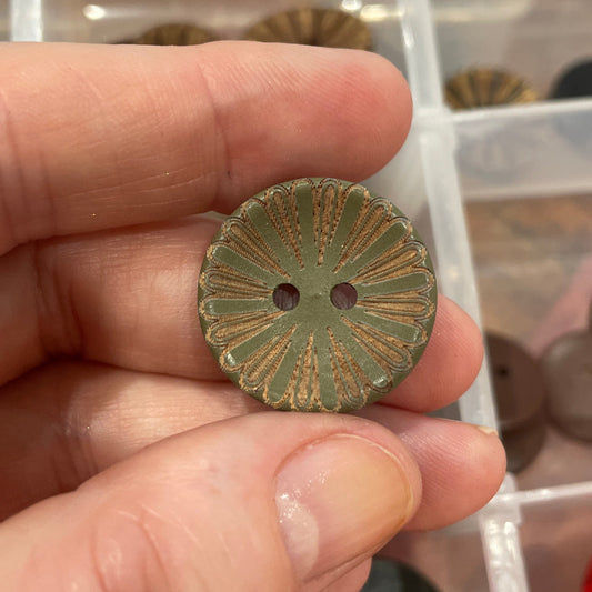Hand holding a decorative button with a clear container of buttons in the background