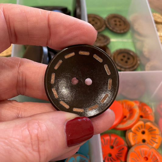 Hand holding a black button with a collection of colorful buttons in the background.