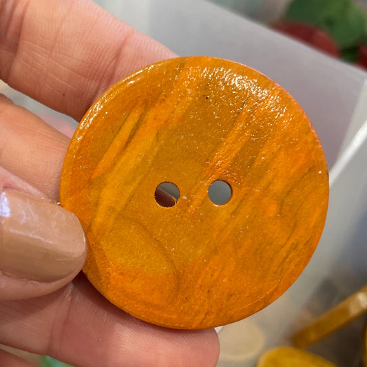 Hand holding a round orange button with a blurred background of more buttons.