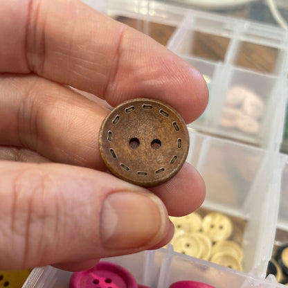 Hand holding a bronze button with pink buttons in a container in the background