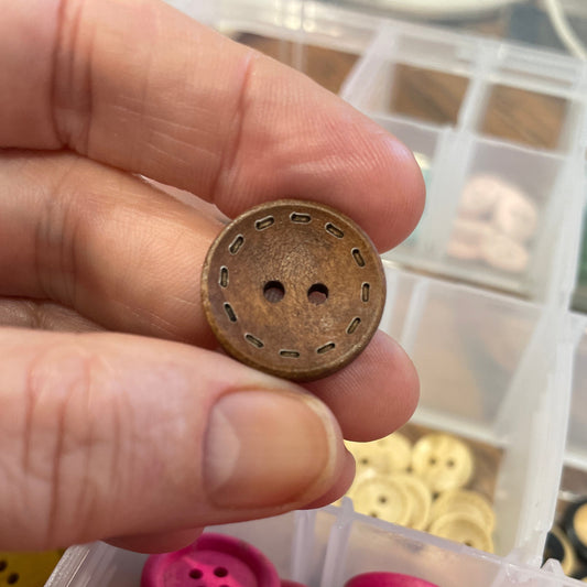 Hand holding a bronze button with pink buttons in a container in the background