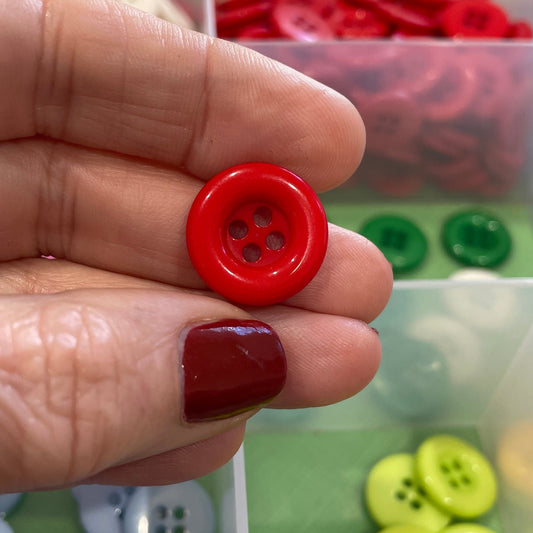 Red button held between fingers with a container of colorful buttons in the background