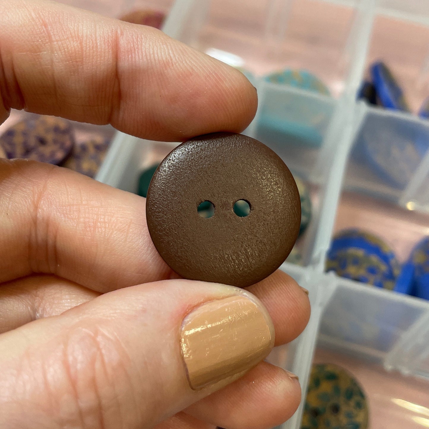 Brown button held by a hand with a clear container of buttons in the background