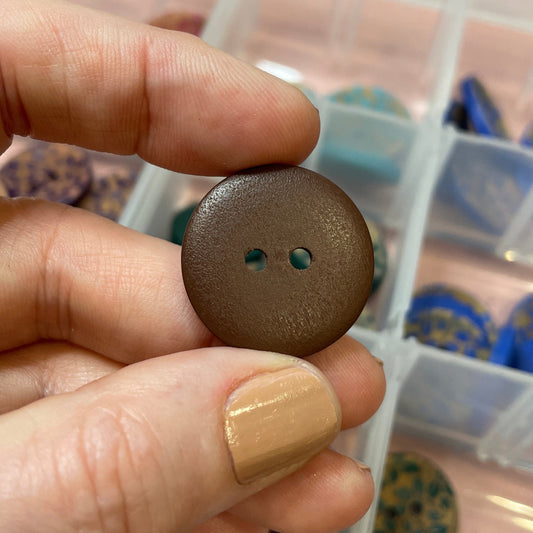 Brown button held by a hand with a clear container of buttons in the background
