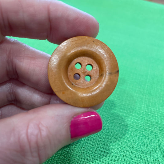 Wooden button held between fingers against a green background