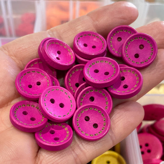 Hand holding pink buttons with a container of buttons in the background