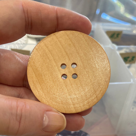 Hand holding a gold button with a clear plastic organizer in the background