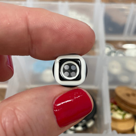 Close-up of a hand holding a black and white button with a container of buttons in the background.