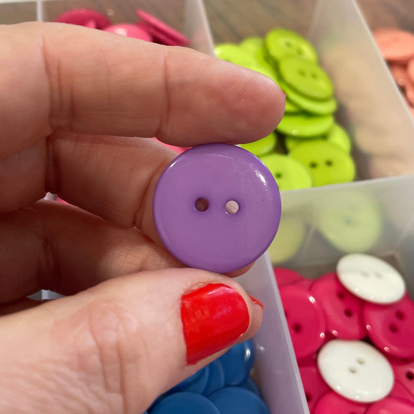 Hand holding a purple button with a background of colorful buttons in a container.