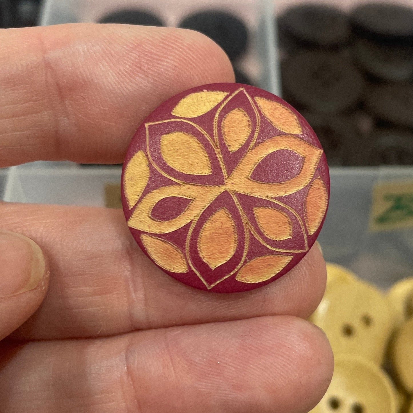 Hand holding a decorative button with a floral pattern, against a background of various buttons.