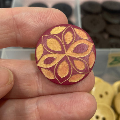 Hand holding a decorative button with a floral pattern, against a background of various buttons.