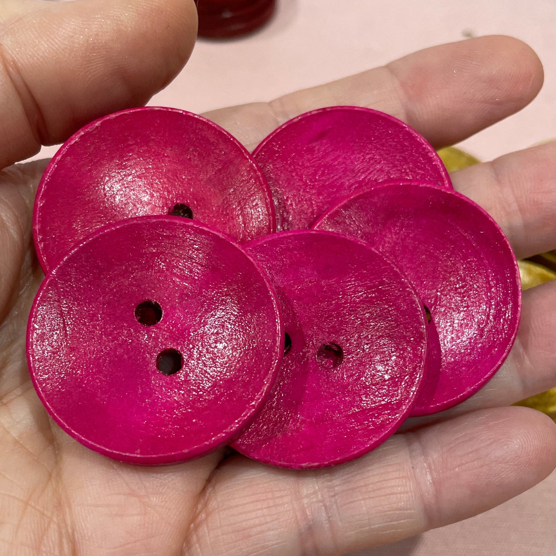 Hand holding pink buttons with a laptop and green button in the background