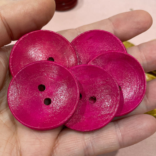 Hand holding pink buttons with a laptop and green button in the background