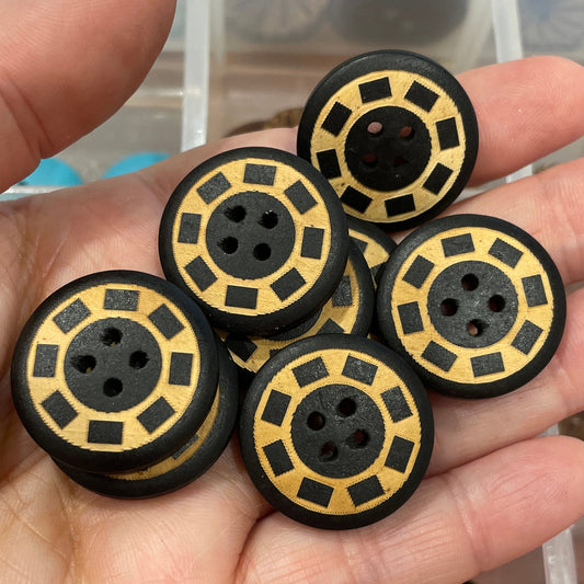 Hand holding black and gold spool-like objects with a clear container of similar items in the background.