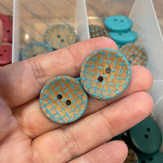Hand holding two decorative buttons with a container of buttons in the background
