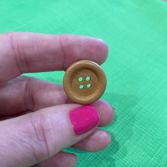 Hand holding a wooden button against a green background