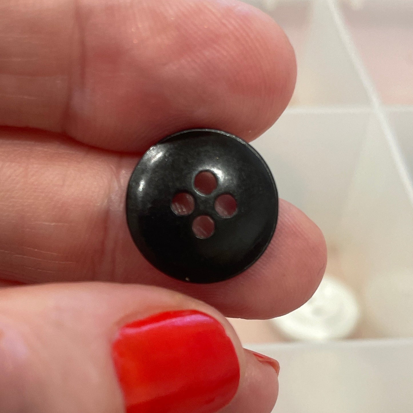 Black button held between fingers with red nail polish on a blurred background