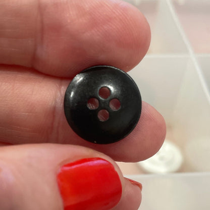 Black button held between fingers with red nail polish on a blurred background