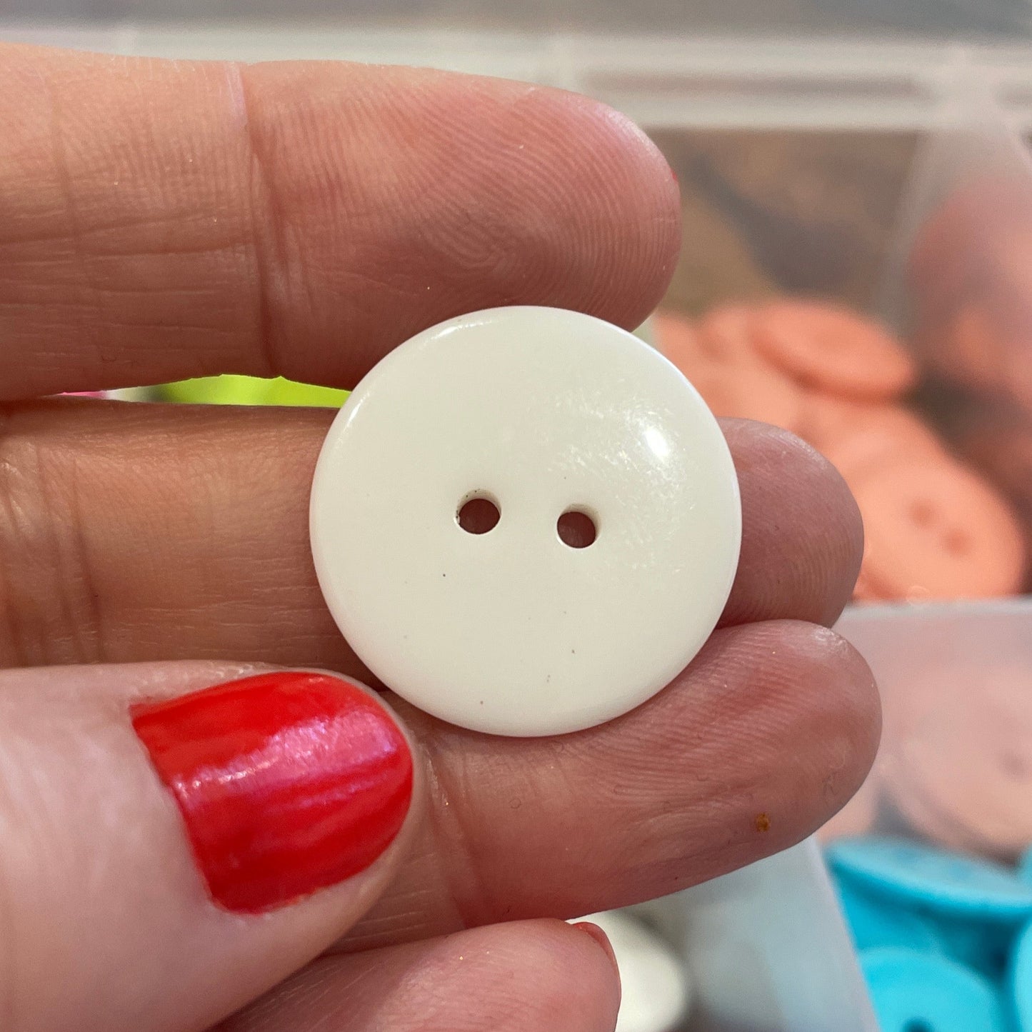 White button held between fingers with colorful buttons in the background