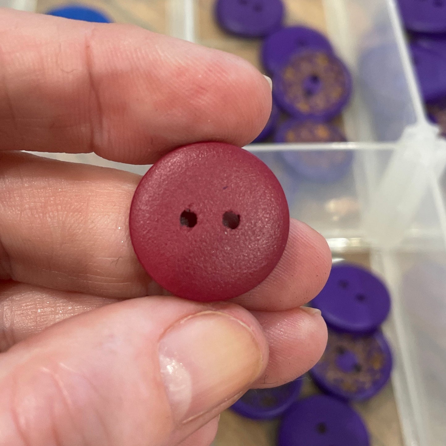 Hand holding a red button with a clear container of purple buttons in the background