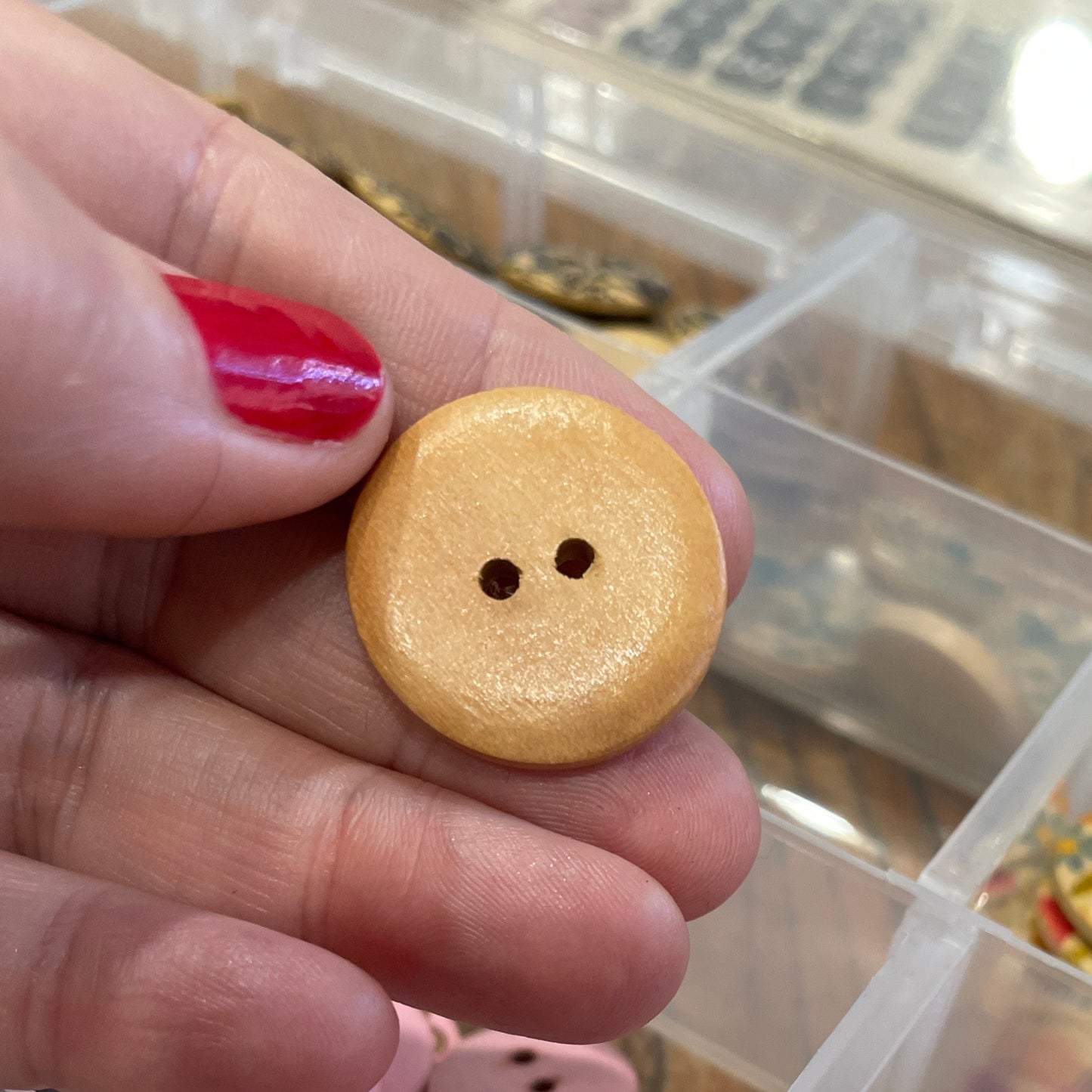 Hand holding a wooden button with a container of colorful buttons in the background