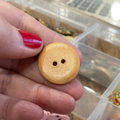 Hand holding a wooden button with a container of colorful buttons in the background