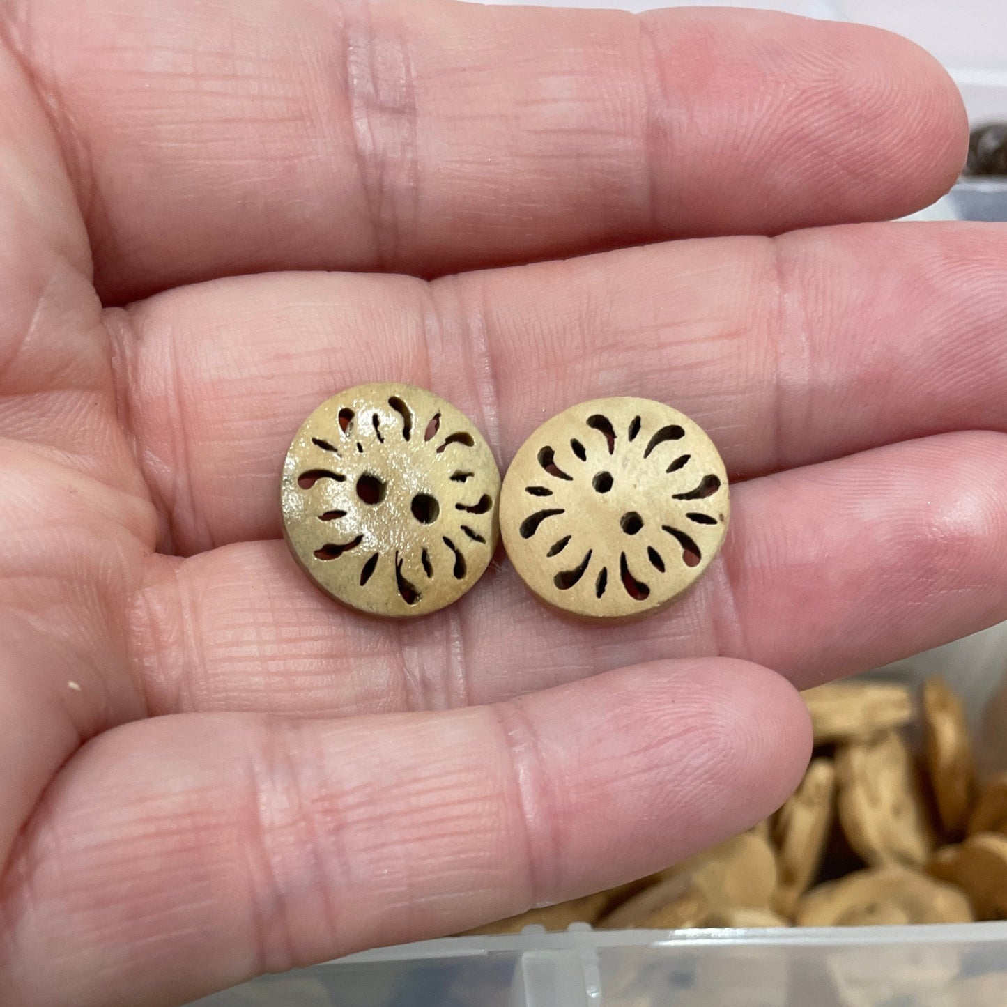 Gold buttons held in a hand with a container of green buttons in the background