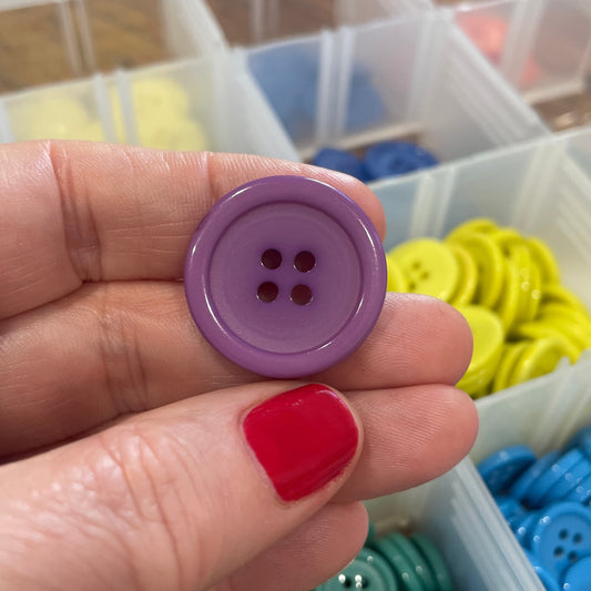Hand holding a purple button with a container of colorful buttons in the background