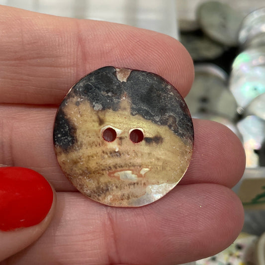 Hand holding a decorative button with a blurred background of button collection