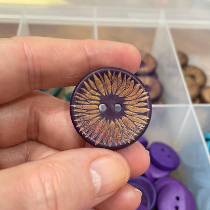 Hand holding a decorative button with a container of buttons in the background