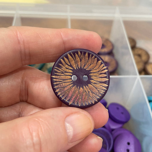 Hand holding a decorative button with a container of buttons in the background