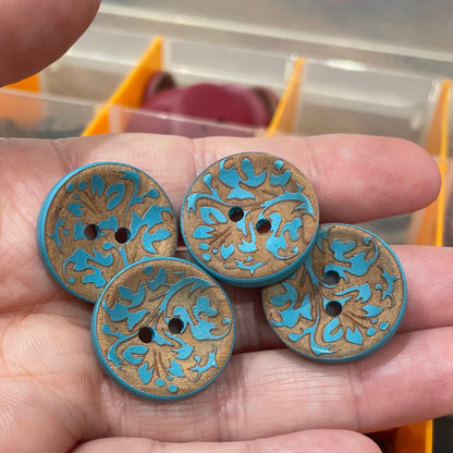 Hand holding four decorative buttons with blue and gold patterns against a blurred background.