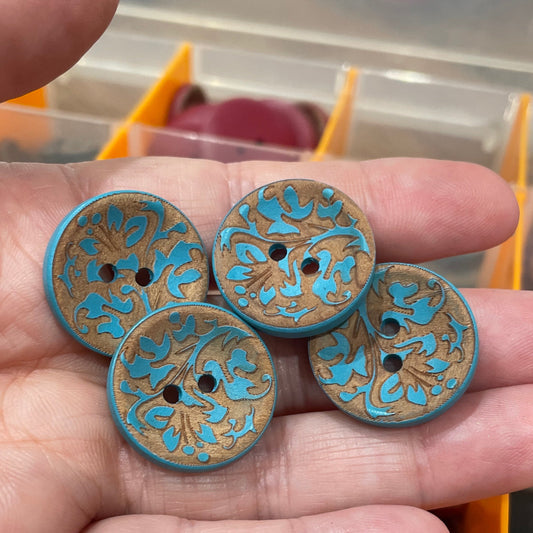 Hand holding four decorative buttons with blue and gold patterns against a blurred background.