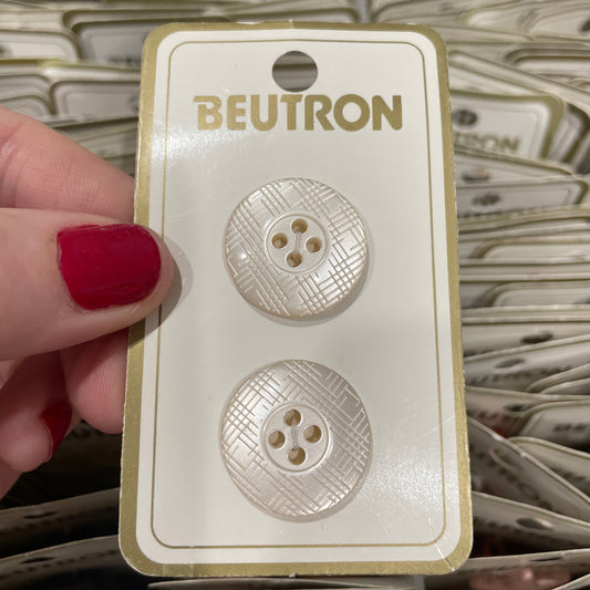 Two buttons on a BEUTRON card held by a hand with red nail polish.