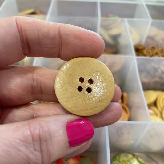 Gold button held by a hand with pink nail polish, against a background of various buttons.