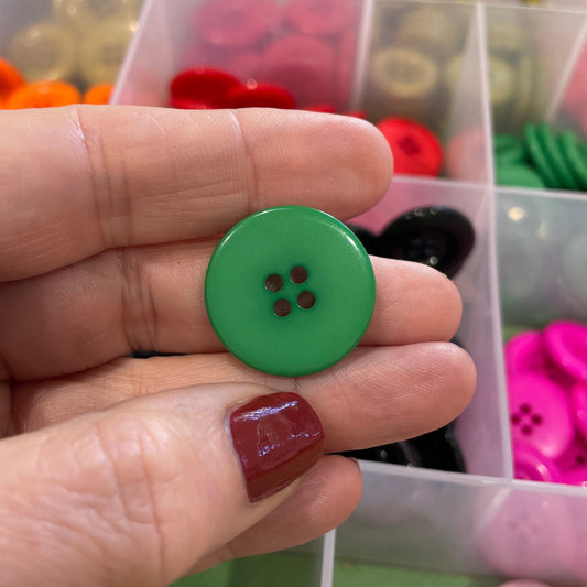 Hand holding a green button with a clear container of assorted buttons in the background