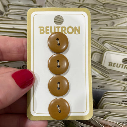 Set of brown buttons on a 'Beltron' card held by a hand with red nail polish.