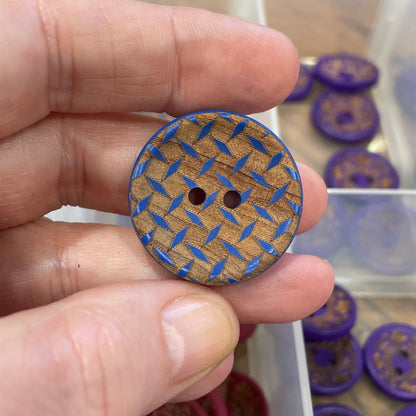 Hand holding a blue textured button with a clear container of buttons in the background
