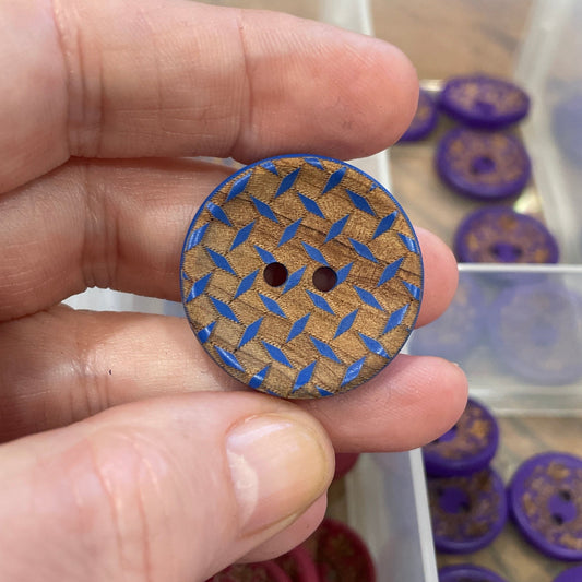 Hand holding a blue textured button with a clear container of buttons in the background