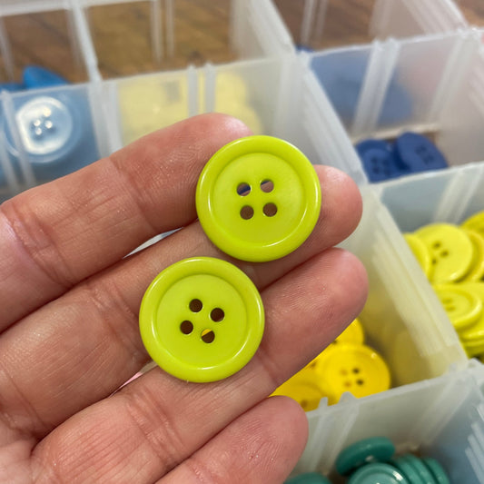 Hand holding two green buttons with a background of colorful buttons in containers.