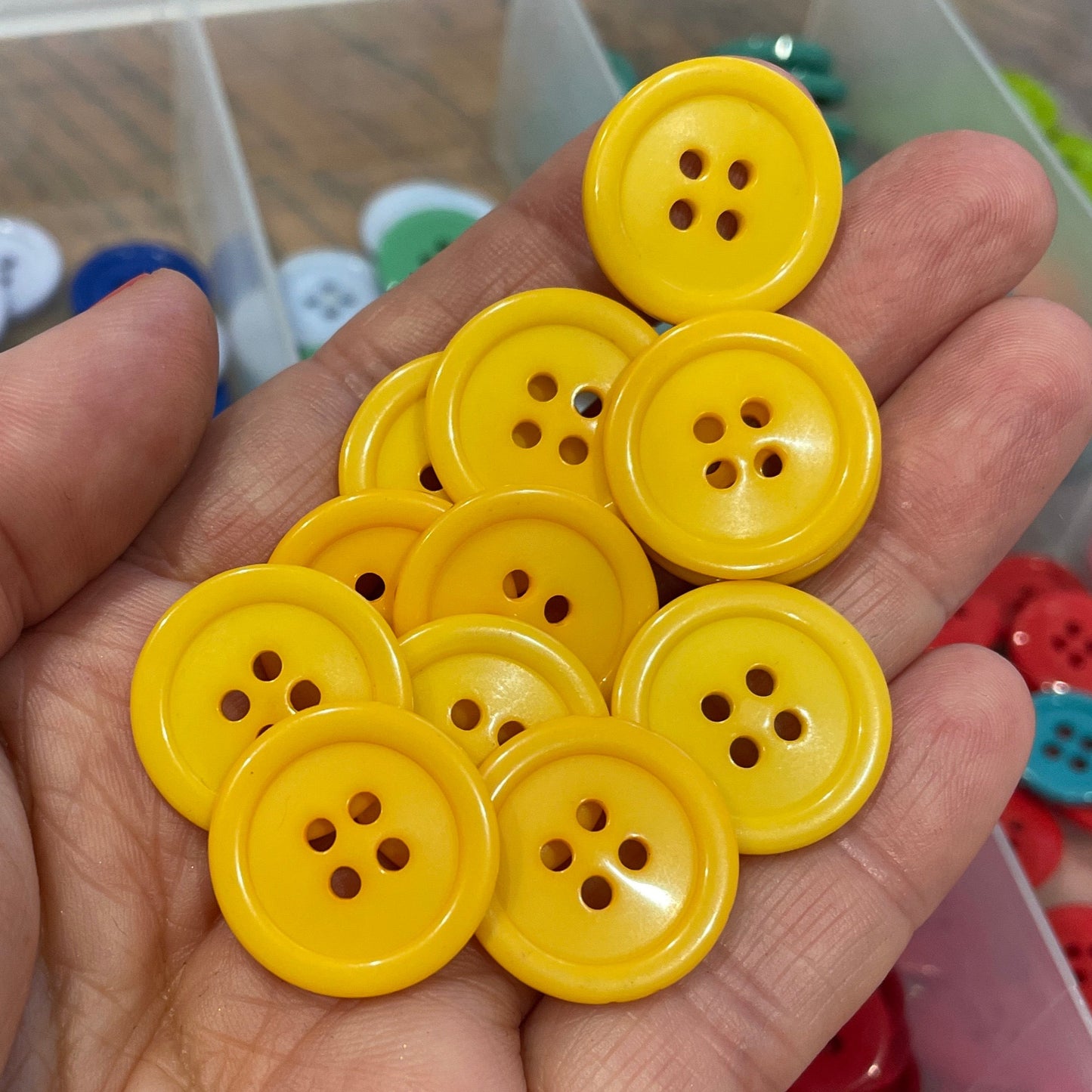 Hand holding yellow buttons with a container of assorted buttons in the background