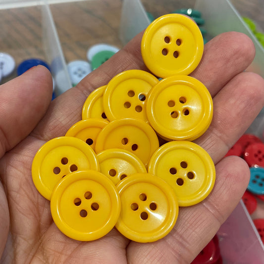 Hand holding yellow buttons with a container of assorted buttons in the background