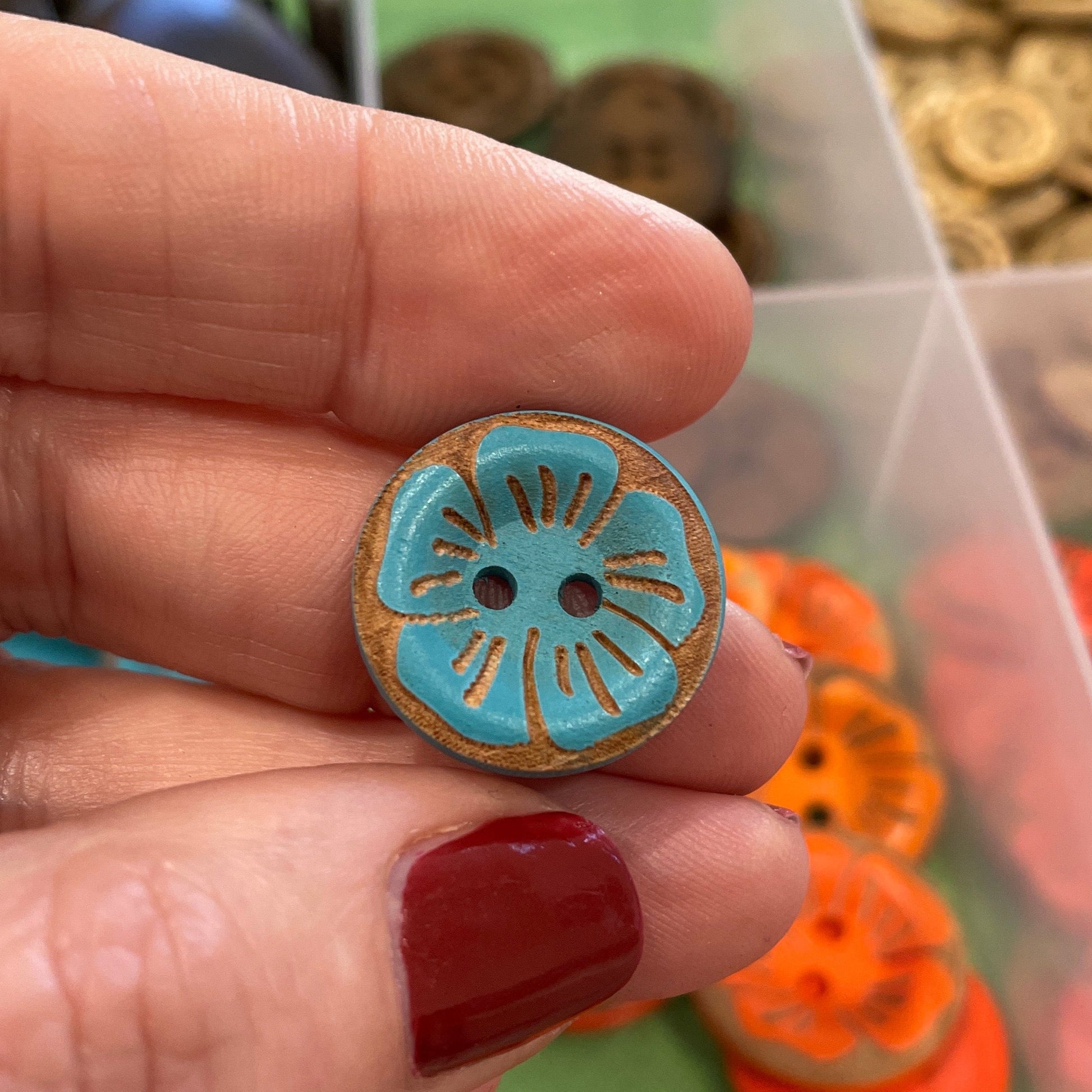 Hand holding a decorative button with a colorful background of button assortments.
