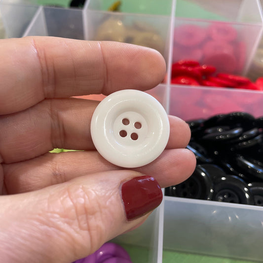 Hand holding a white button with a colorful assortment of buttons in the background
