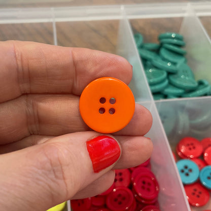 Hand holding an orange button with a container of colorful buttons in the background