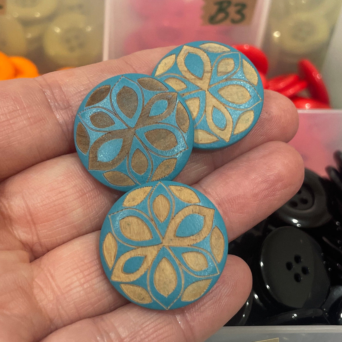 Hand holding decorative buttons with a colorful button organizer in the background