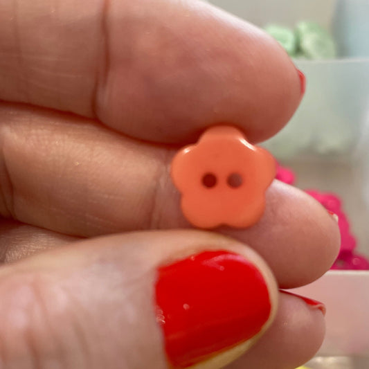 Hand holding two small flower-shaped buttons with a blurred background of more buttons.